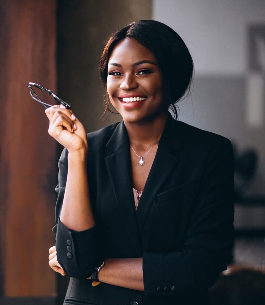 A young african business woman is smiling and holding her glasses.