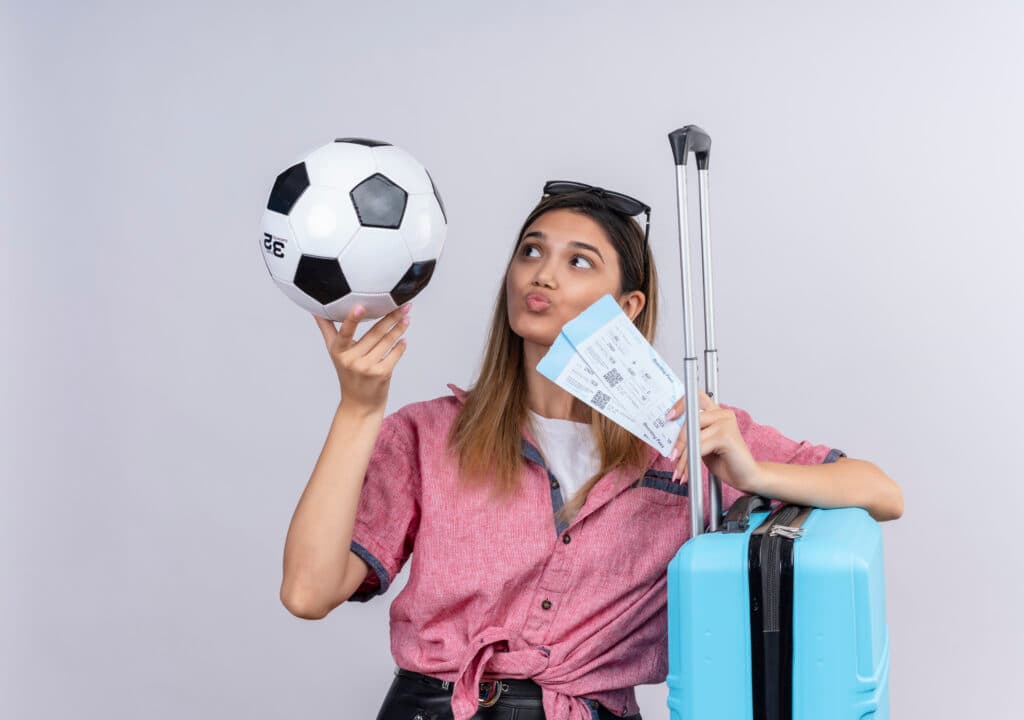Young woman with sunglasses holding a soccer ball, plane tickets and a suitcase