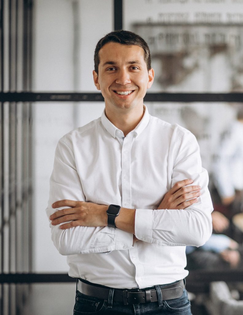 A smiling businessman in a white shirt standing in an office.