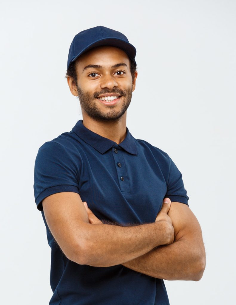 Um jovem de camisa pólo azul com os braços cruzados sobre um fundo branco.