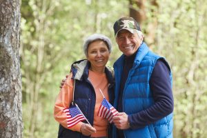 Um casal mais velho segurando bandeiras americanas na floresta.