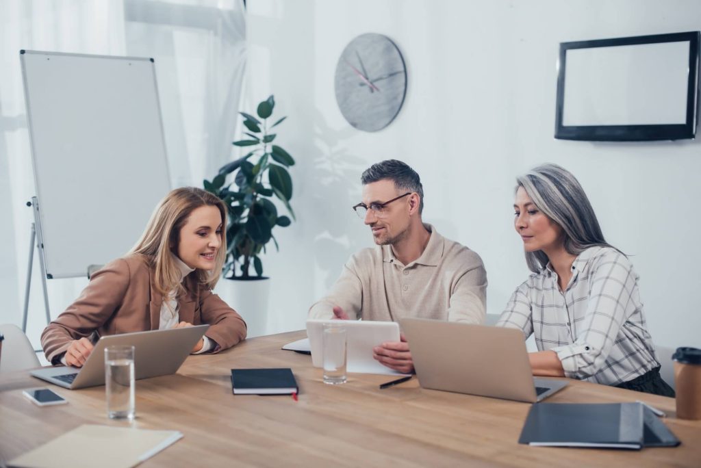 Um grupo de pessoas sentadas ao redor de uma mesa com laptops.