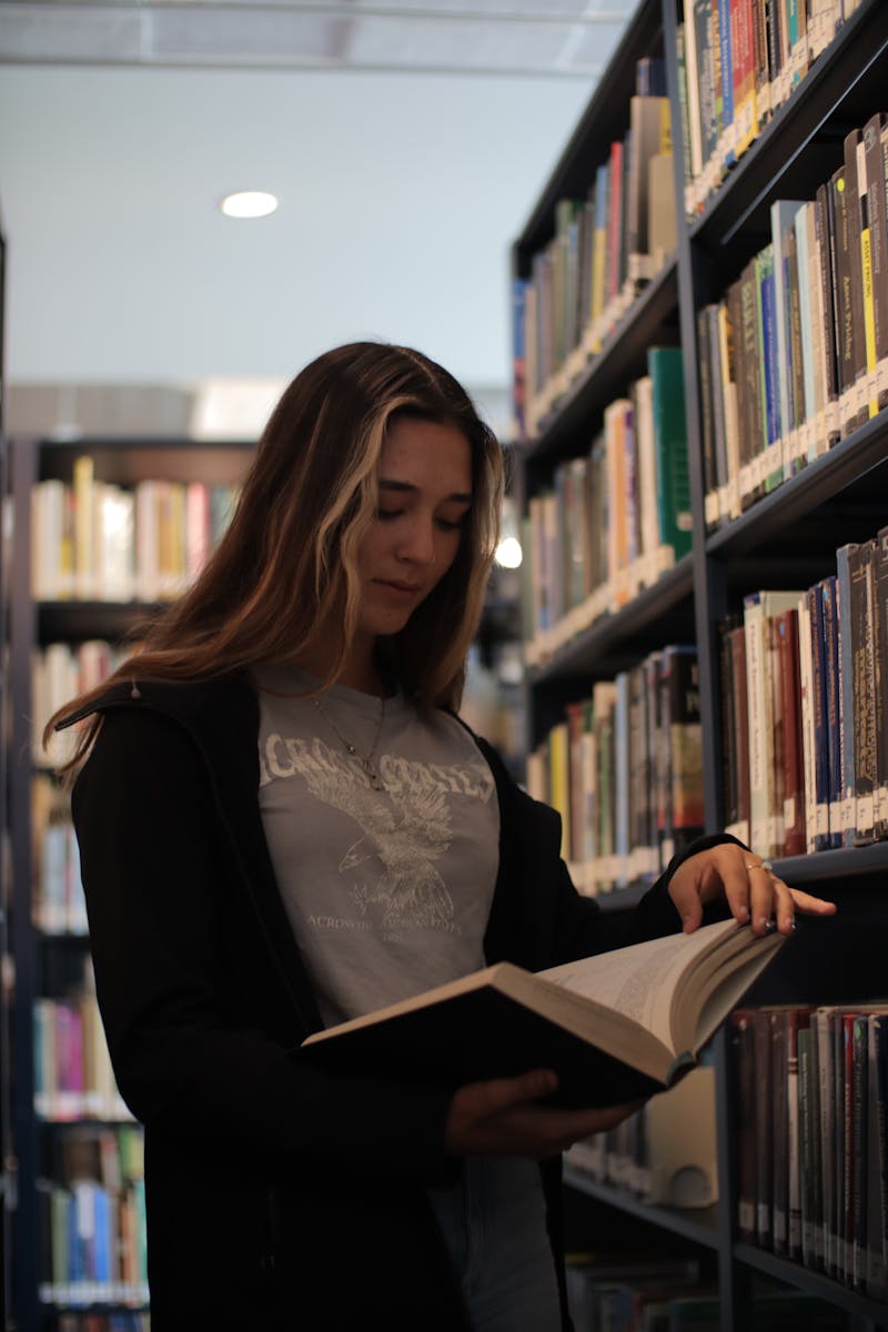 A woman is standing in a library looking at a book