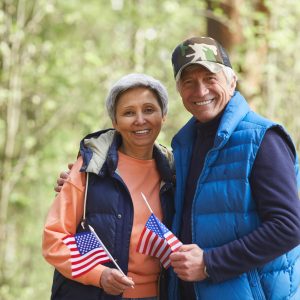 Um casal mais velho segurando bandeiras americanas na floresta.